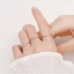 Conjunto de três anéis finos com detalhes de estrelas e lua, usados na mão de uma pessoa com pele clara e vestindo uma manga branca.