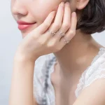 Anel de prata delicado com pedras brilhantes, usado na mão de uma mulher com unhas bem cuidadas, em um fundo neutro.