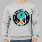 Sweatshirt cinza com logotipo Falcon Heavy SpaceX, ilustração de um foguete em lançamento num estilo gráfico moderno, ideal para entusiastas do espaço e tecnologia.