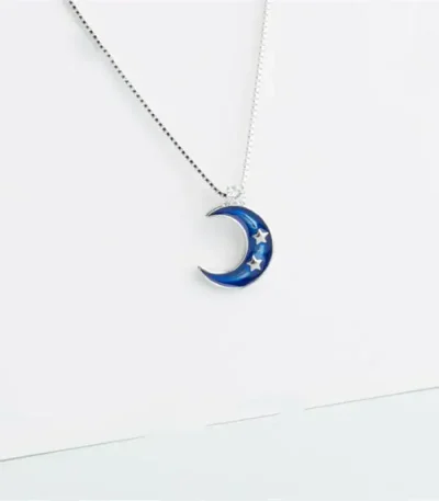 Pingente em forma de lua azul com estrelas, suspenso em uma corrente fina.