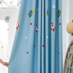 Cortina azul com desenhos de foguetes, planetas e estrelas, decorando um quarto infantil com tema espacial.