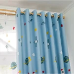 Cortina azul com desenhos de planetas, estrelas, foguetes e satélites, decorando uma janela de quarto infantil com luz natural.