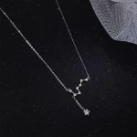 Colar delicado com pingente em forma de constelação de estrela, em prata, suspenso em uma fina corrente, colocado sobre um fundo preto com um tecido de malha.