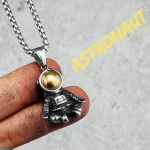 Colar com pingente de astronauta em metal prateado e bola dourada, inspirado no espaço e na exploração espacial.