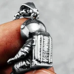 Pendentif em forma de astronauta em metal prateado, detalhado com um capacete e um mochila, perfeito para os amantes de espaço e de ciência.