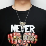 Pingente científico em forma de crânio e punho fechado com inscrição "BOSS" em letras douradas, usado com uma corrente de metal prateado.