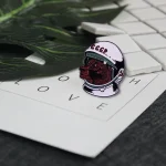 Carimbo em forma de cabeça de lobo usando um capacete espacial com inscrição "CCCP", colocado sobre uma folha com as letras "LOVE" e peças de xadrez ao fundo.