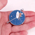 Um broche representando uma estação espacial com antenas e painéis solares, ideal para os amantes de astronomia e decoração científica.