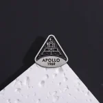 Peça de decoração em forma de logotipo Apollo 1969, inspirada na missão espacial, colocada sobre uma superfície branca com fundo preto.