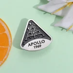 Pingente em metal representando a missão Apollo 11 de 1969 com a silhueta da lua.