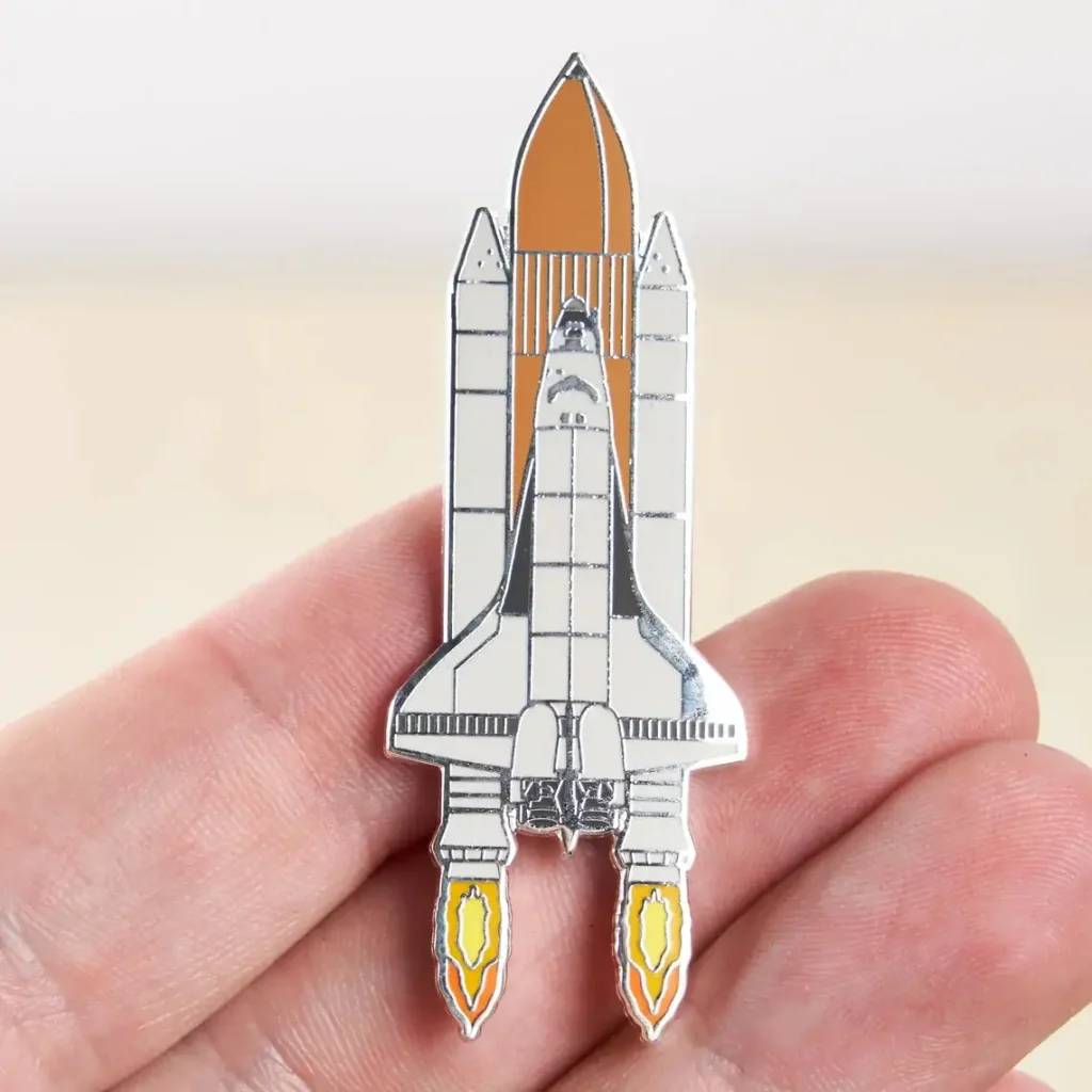 Pin em forma de nave espacial com detalhes em metal, ilustrando um foguete pronto para decolar, perfeito para os amantes de astronomia e ciência.