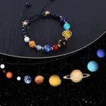 Pulseira com beads representando planetas do sistema solar e estrelas, incluindo a Terra, Saturno, Júpiter, e estrelas douradas, sobre fundo escuro com tema espacial.