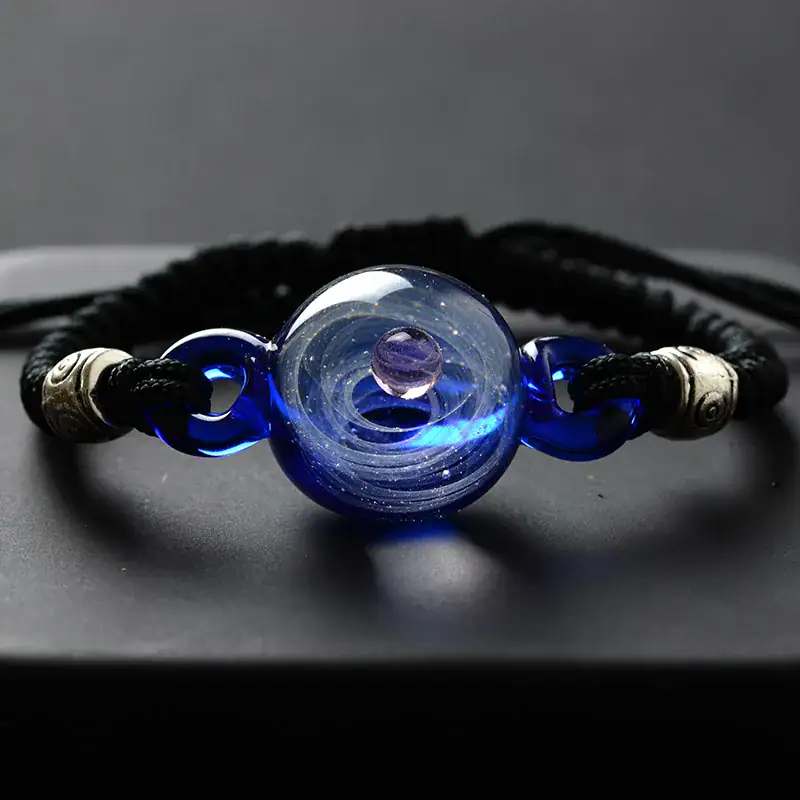Pulseira de cordão negro com esfera de vidro azul e detalhes metálicos.
