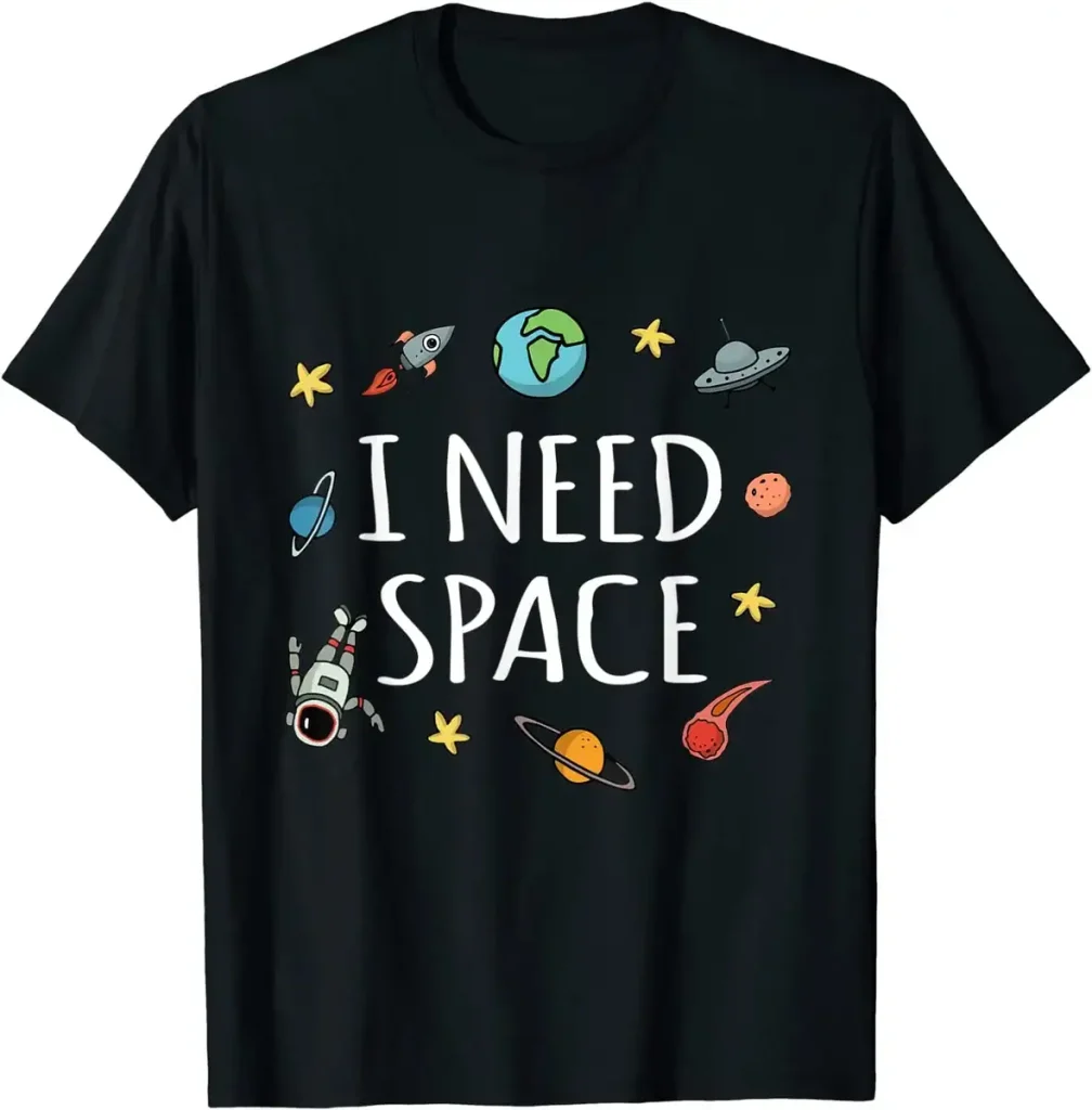 Confira esta camiseta preta com o texto "I NEED SPACE" cercado por desenhos de planetas, astros, um foguete, um astronauta e um disco voador, perfeito para os amantes de astronomia e ciência.