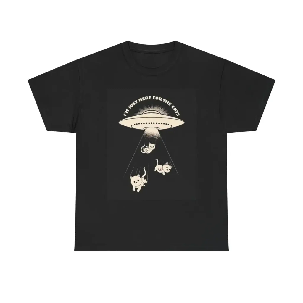 T-shirt preta com ilustração de um OVNI e três animais sob um feixe de luz, texto "I must here for the cake" no topo.