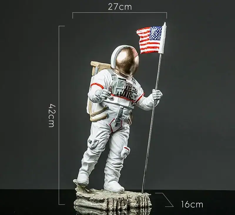 Vêtement d'astronaute avec drapeau américain Vêtement d'astronaute en figurine avec drapeau américain, hauteur 42 cm, dimensions 27x16 cm, représentant un explorateur spatial en tenue complète, debout sur une base rocheuse.