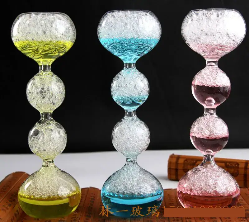 Balançoire en verre coloré avec bulles d'air Balançoire en verre coloré avec bulles d'air, composée de trois segments en forme de boule, chacun rempli de liquide coloré (jaune, bleu, rose) et de bulles d'air, sur fond noir.
