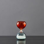 Balancier de sablier en verre rouge et transparent avec sable blanc.