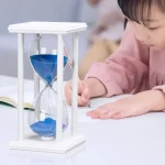 Relógio de areia com moldura em madeira branca e areia azul, usado como objeto educativo ou decoração científica.