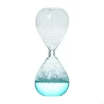 Ampulheta de vidro transparente com líquido azul e grãos brancos, símbolo do tempo que passa, ideal para decoração científica ou educativa.