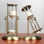 Ampulheta decorativa em vidro com moldura em metal dourado, estilo vintage, para decoração de ciência ou escritório.