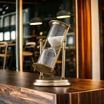 Ampulheta decorativa em metal vintage com vidro transparente, ideal para decoração interior ou como objeto de coleção.