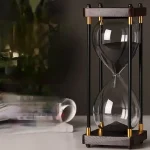 Ampulheta científica em vidro com estrutura de madeira e elementos metálicos dourados, ideal para decoração de escritório ou prateleira com estilo industrial ou científico.