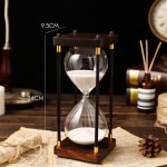 Ampulheta decorativa em madeira e vidro, mede 24 cm de altura e 9,5 cm de largura, ideal para decoração científica ou como objeto de coleção.