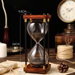 Ampulheta decorativa em madeira e vidro com areia preta, mede 24 cm de altura e 9,5 cm de largura, ideal para decoração científica ou vintage.