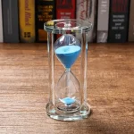 Ampulheta de vidro com areia azul, símbolo da medição do tempo, ideal para decoração científica ou educativa.
