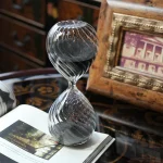 Ampulheta de vidro transparente com grãos de areia pretos, decoração elegante e vintage para um interior sofisticado.