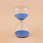 Ampulheta em vidro transparente preenchida com areia azul, símbolo do tempo que passa, ideal para decoração científica ou educativa.