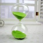 Ampulheta em vidro com areia verde, símbolo da medição do tempo, ideal para decoração científica ou educativa.