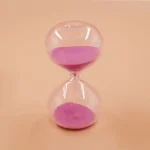 Ampulheta em vidro transparente contendo areia rosa, símbolo de tempo e paciência, ideal para decoração científica ou educativa.