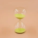 Ampulheta em vidro transparente com areia verde, símbolo de tempo e paciência, ideal para decoração científica ou como objeto de coleção.
