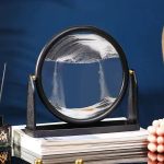 Peso de papel circular em vidro com líquido, decoração científica elegante, colocado sobre uma pilha de livros, ideal para decoração de escritório ou prateleira.