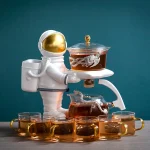 Um astronauta de plástico branco com capacete dourado, segurando uma bandeja com um recipiente contendo um líquido marrom, rodeado de várias xícaras de vidro com líquido semelhante.