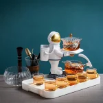 Decoração de chá original com um astronauta em cerâmica servindo chá quente, rodeado de xícaras e acessórios de cozinha, sobre fundo azul.