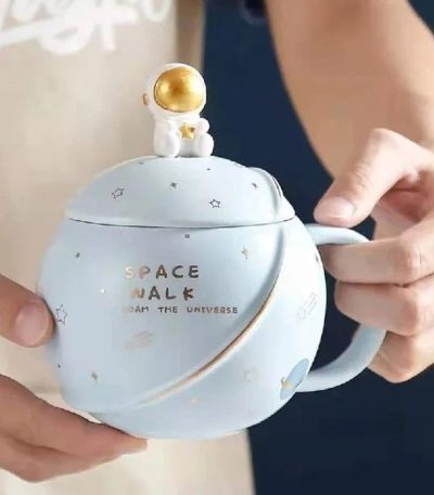 Caneca de cerâmica com motivo espacial e figura de astronauta dourado na tampa, ideal para decoração ou consumo de bebidas inspiradas no espaço.