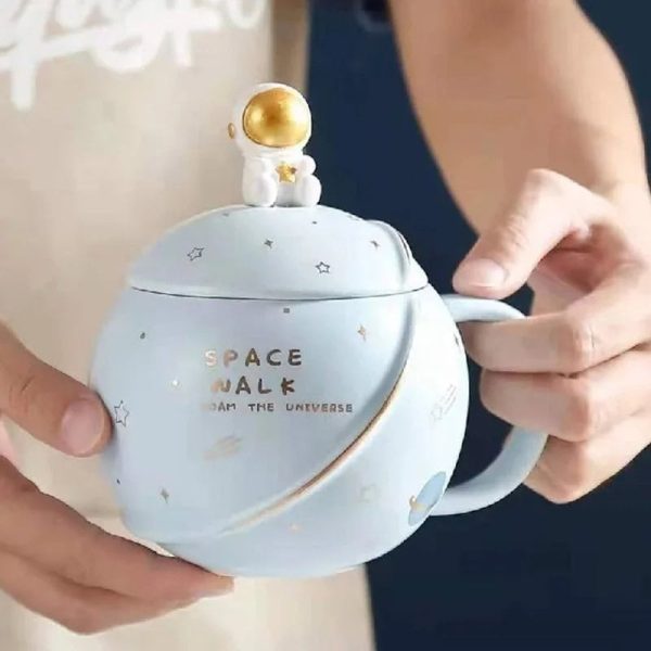 Caneca de cerâmica com motivo espacial e figura de astronauta dourado na tampa, ideal para decoração ou consumo de bebidas inspiradas no espaço.