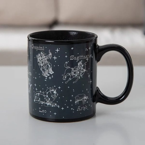 Caneca de cerâmica preta com ilustrações das constelações do zodíaco: Gêmeos, Sagitário, Leão, Áries, e mais, com nomes em francês.