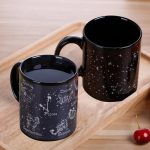 Duas canecas pretas com padrões de astros, constelações e signos do zodíaco, perfeitas para os amantes de astronomia e decoração científica.