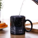Caneca de cerâmica preta com ilustrações de constelações do zodíaco, Leão e Áries, sob um céu estrelado, ideal para os amantes de astronomia e decoração científica.