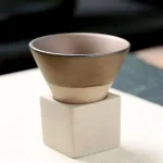 Pequeno pote em cerâmica bege colocado sobre um pedestal de concreto branco, ideal para decoração científica ou de escritório.