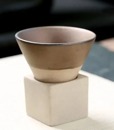 Pequeno pote em cerâmica bege colocado sobre um pedestal de concreto branco, ideal para decoração científica ou de escritório.