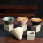 Três canecas em cerâmica com padrões coloridos e design moderno, colocadas sobre suportes de concreto, sobre uma superfície de madeira, ilustrando um objeto de decoração científica.