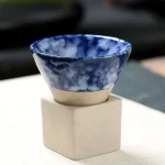 Pequena caneca em cerâmica com padrão marmoreado azul e branco, colocada sobre um suporte de concreto, ideal para decoração científica ou para uso prático.