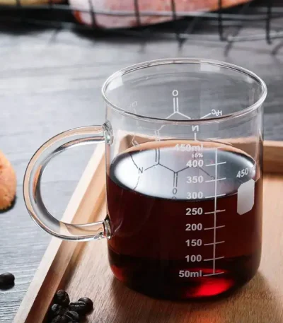Caneca de laboratório em vidro contendo um líquido escuro, graduada para medir precisamente o volume, ideal para experiências científicas ou decoração temática.