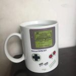 Caneca em forma de console Game Boy com ecrã exibindo "Super Mario Land" e botões coloridos, ideal para fãs de videojogos retro.