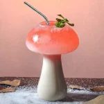 Copo em forma de cogumelo contendo um cocktail rosa com um ramo de hortelã, decorativo e original.